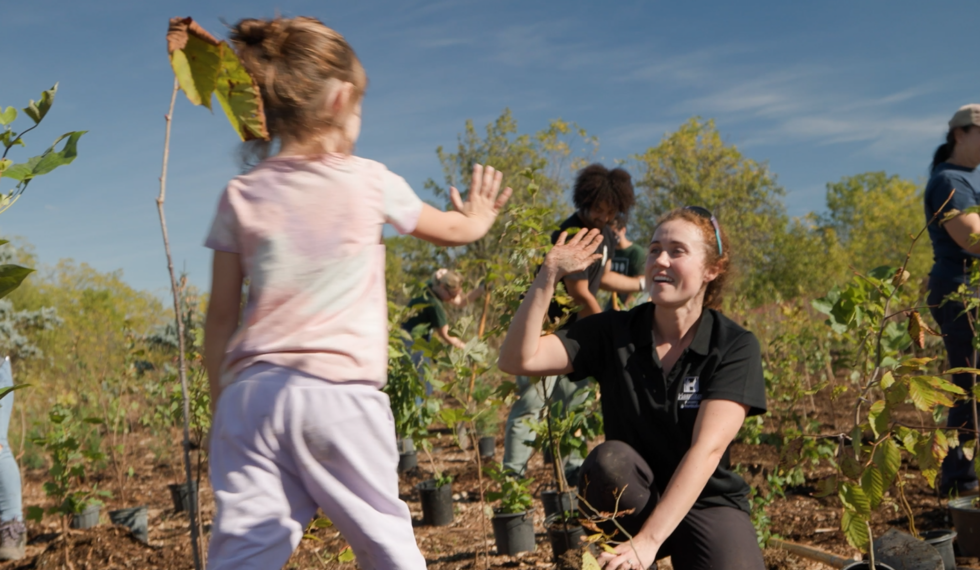 a child high fiving a kneeling adult after helping to plant trees