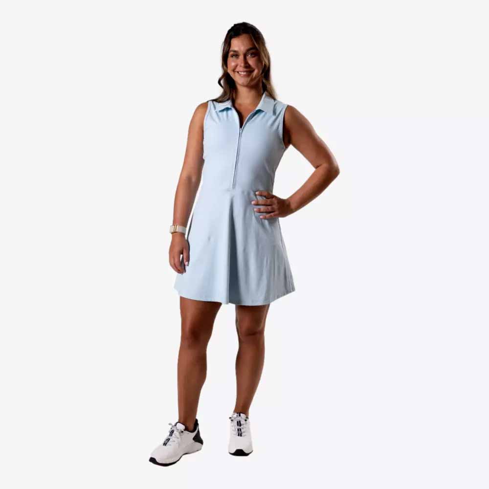 A woman stands smiling with one hand on her hip, wearing stylish apparel&mdash;a light blue sleeveless dress and white sneakers&mdash;against a plain white background, perfect for a Mother's Day look.