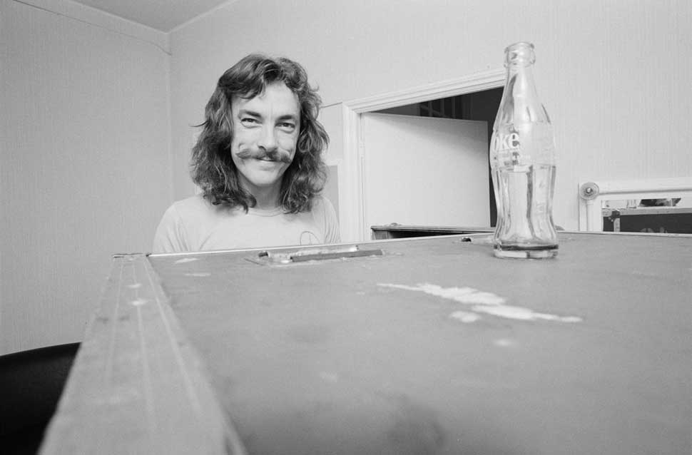 Neil Peart in 1979 sitting behind a flightcase, smiling at the camera