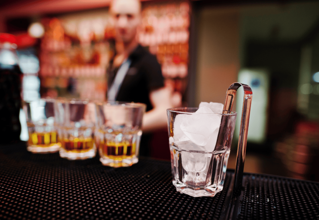 Glass with ice and tongs with three whiskey glasses background barman
